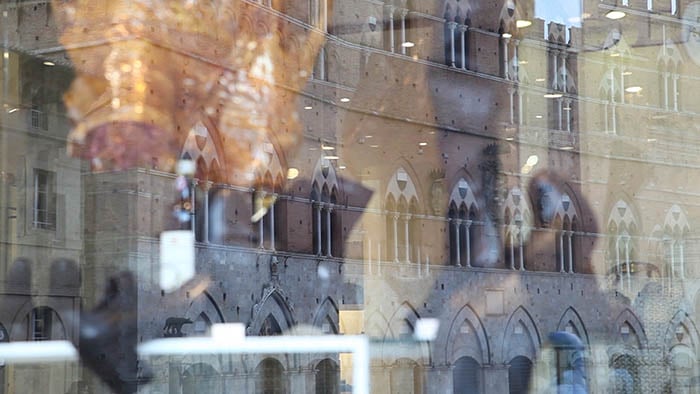 A view of Palazzo pubblico, reflected in a shop window in piazza del Campo. Wedding videographer Tuscany: A view of Palazzo pubblico, reflected in a shop window in piazza del Campo.